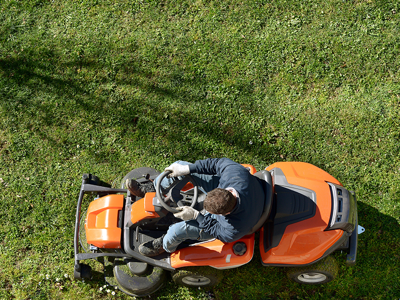 top view of man operating an orange riding lawn mower